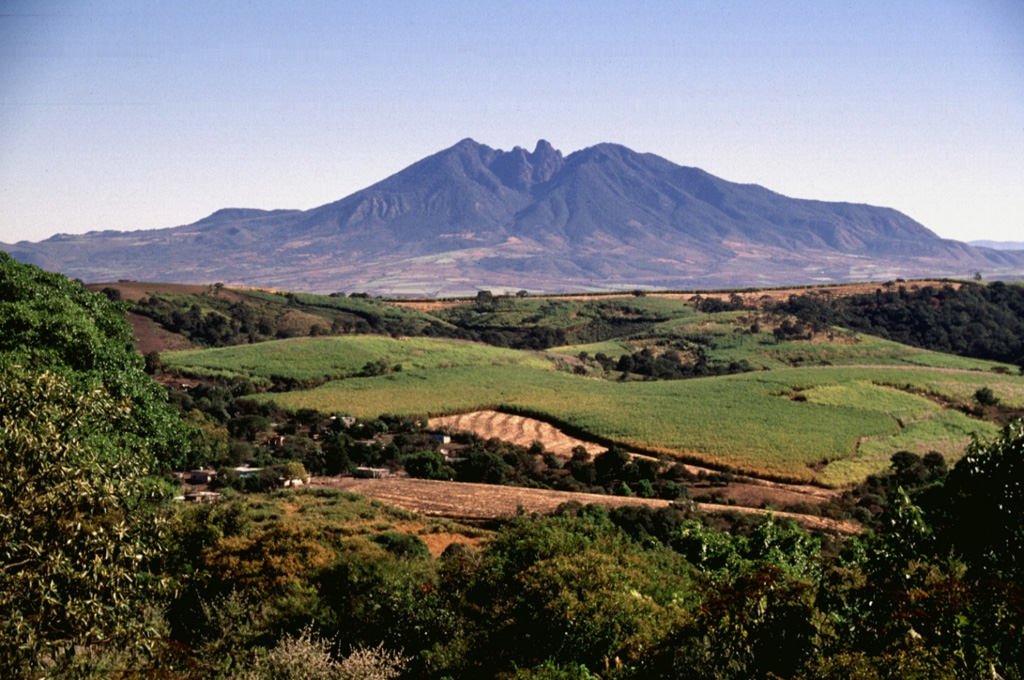 Sangangüey is an eroded stratovolcano that is seen here from the SW across farmlands of the Tepic basin, with a spine visible in the summit crater. The NW and SE flanks contain 45 scoria cones that erupted during the past 300,000 years; some of these NW-flank cones are visible below the left horizon.  Photo by Lee Siebert, 1997 (Smithsonian Institution).