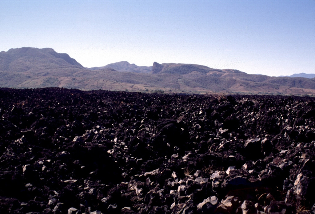 Highway 15 cuts across the lava flow that extends 7 km down the SW flank of Ceboruco. Maps show that this flow, referred to as El Ceboruco, existed prior to the 1870 eruption. Pliocene ignimbrites form the hills in the background. Photo by Lee Siebert, 1997 (Smithsonian Institution).