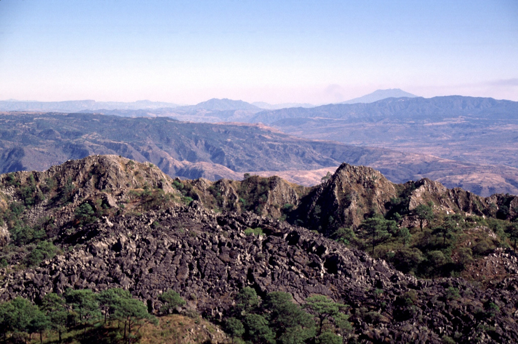 The inner caldera rim of Ceboruco forms the ridge extending across the photo in this view looking toward the SE from near the summit. The inner caldera wall consists of massive dome lavas that were emplaced within the outer caldera. The unvegetated lava flow in the foreground was erupted from a vent within a scoria cone complex at the western side of the inner caldera, probably in 1870. Flat-topped Volcán Tequila forms the peak in distance to the upper right. Photo by Lee Siebert, 1997 (Smithsonian Institution).