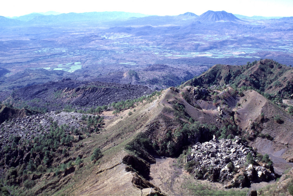 The view of the 1870 vent and the San Pedro-Ceboruco graben is from the Ceboruco summit. The small lava dome to the lower right and the unvegetated lava flow to the lower left were emplaced during the 1870-75 eruption. The Cerro San Pedro lava dome on the horizon directly above the 1870 dome was constructed within the 7 x 10 km San Pedro caldera. The peak immediately left of Cerro San Pedro is Cerro Tetillas. Photo by Lee Siebert, 1997 (Smithsonian Institution).