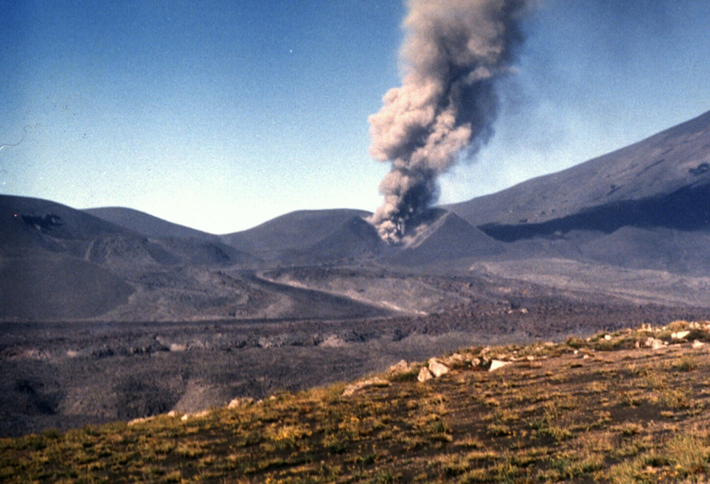 A lava flow in the foreground issues from the breached Navidad cinder cone on February 8, 1989, while an ash plume rises above the crater.  The lava flow originated on December 27, 1988, two days after the start of the eruption from a vent on the NE flank of Lonquimay volcano, whose slope is visible at the right.  The flow advanced rapidly during the first few days of the eruption, reaching 4 km by Janaury 2.  It then slowed, and by the time the eruption ended, in January 1990, the blocky lava flow reached 10 km down the Río Lolco valley. Photo by Hugo Moreno, 1989 (University of Chile).