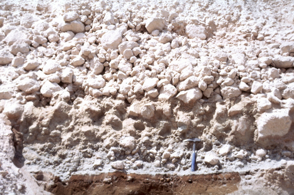 A pyroclastic flow deposit from the 1929 eruption of Komagatake volcano, on the northern Japanese island of Hokkaido, overlies a brown pre-eruption surface. The upper part of the deposit contains large pumice that lacks fine-grained material between the clasts and the underlying unit is enriched in fine-grained material. A geological hammer provides scale. Photo by Shinji Takarada, 1992 (Geological Survey of Japan).