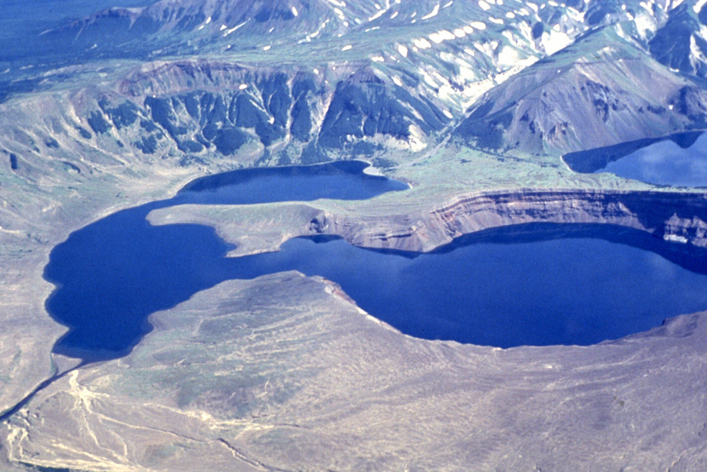 A major explosive eruption about 1,800 years ago produced 10-15 km3 of tephra, including widespread pyroclastic flows, associated with formation of the 3.5 x 4.5 km Ksudach V caldera. The NE caldera wall forms the cliff to the upper left. Soon after this eruption, about 1,600 years ago, Shtyubel' cone began growing in the center of the caldera. A major eruption in 1907 created three large NE-SW-trending maar craters in the center of the photo. The craters have been largely filled by a lake. Photo by Nikolai Smelov, 1996 (courtesy of Vera Ponomareva, Institute of Volcanic Geology and Geochemistry, Petropavlovsk).