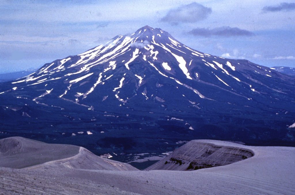 Zheltovsky rises across a valley NE of Iliinsky volcano. The flat shelf on the right flank is the eastern rim of a 4 x 5 km, largely buried Pleistocene caldera. The western rim of a smaller, late-Holocene caldera forms the break in slope on the left side just below the summit lava dome complex. The crater in the foreground is a NE-flank maar of Iliinsky that formed in 1901. Photo by Nikolai Smelov, 1996 (courtesy of Vera Ponomareva, Institute of Volcanic Geology and Geochemistry, Petropavlovsk).