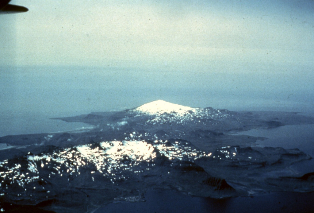 Lýsuhóll, Iceland's smallest volcanic system, consists of small scoria cones and vents in a roughly NW-SE trend along the Snæfellsnes Peninsula in the center of this photo. The cones and vents are seen here from the ENE and are located between the snow-covered Helgrindur mountains in the foreground and the glaciated Snæfellsjökull in the background.  Photo by Thorvaldur Bragason, Iceland Geodetic Survey (courtesy of Richie Williams, U.S. Geological Survey).