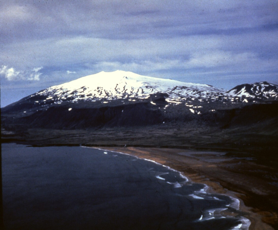 Glaciated Snæfellsjökull towers above Breiðavík bay at the western tip of the Snæfellsnes Peninsula in western Iceland. Numerous cones have formed across the flanks and Holocene lava flows extend across the entire western half of the edifice to the sea. One recent flow that reached the coast on the eastern flank can be seen in the left side of the photo. Photo by Richie Williams, 1979 (U.S. Geological Survey).