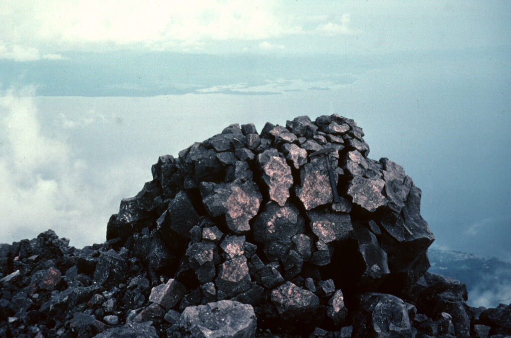 This classic breadcrust bomb was one of many large volcanic bombs ejected during the September 1980 eruption of Gamalama volcano.  Ejected bombs and blocks covered a broad area up to about 1 km from the summit vent, primarily in northern and western directions.  The largest ejected block was about 6 m in diameter.  The western coast of Halmahera Island is visible in the distance. Photo by Jack Lockwood, 1980 (U.S. Geological Survey).
