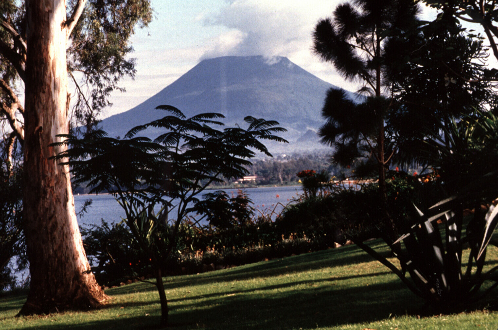 Nyiragongo is seen here from the S across Lake Kivu at Peyer Yard in Rwanda. It contained a lava lake in its deep summit crater that was active for half a century before draining suddenly in 1977. In contrast to the low profile of the nearby Nyamuragira shield volcano, Nyiragongo displays the steep slopes of a stratovolcano. About 100 smaller cones are located primarily along radial fissures east of the summit and along a NE-SW zone extending as far as Lake Kivu. Photo by B. Martinelli, 1994 (courtesy of Jack Lockwood, U.S. Geological Survey).
