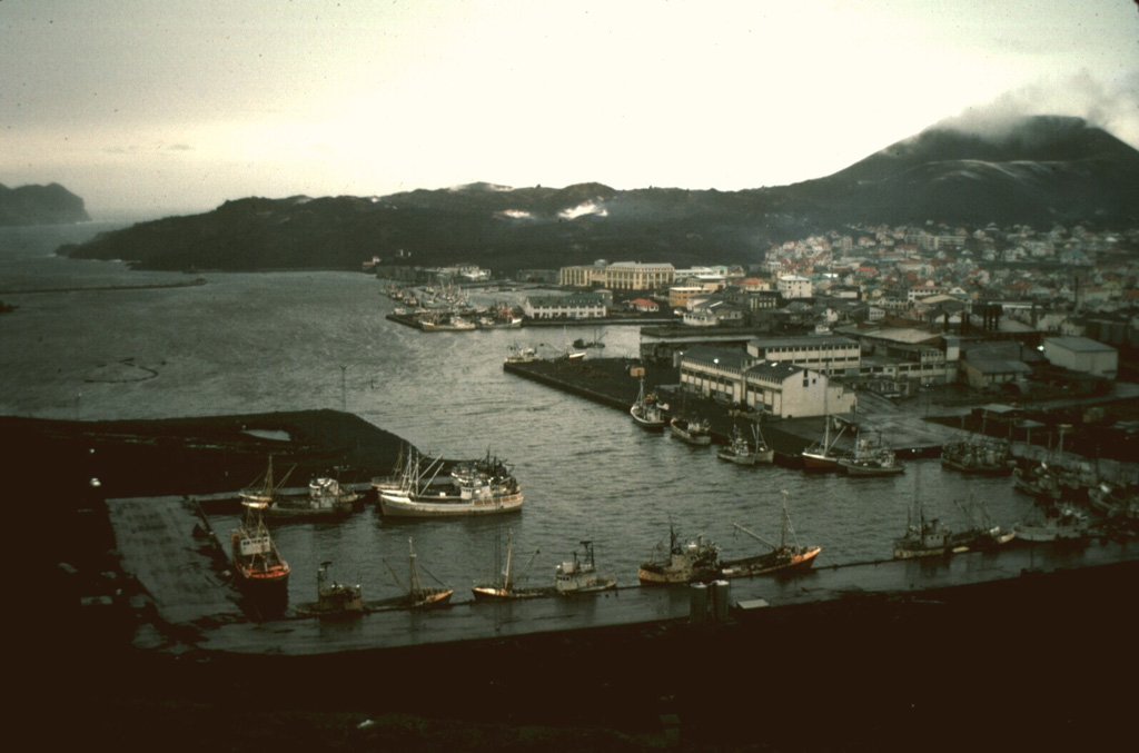The harbor on the island of Heimaey is seen here in 1974, in the aftermath of an eruption that produced a lava flow that almost blocked the harbor entrance. The flow, which originated from a fissure extending from Eldfell cinder cone (upper right) forms the peninsula at the upper left. Extensive water pumping efforts were undertaken to cool and stop the advance of the flow; the diversion attempts were locally successful. The flow eventually stopped, after extending the shoreline up to 1.1 km over a 2.7-km-wide area, providing a more sheltered harbor. Photo by Robin Holcomb, 1974 (courtesy of Jack Lockwood, U.S. Geological Survey).