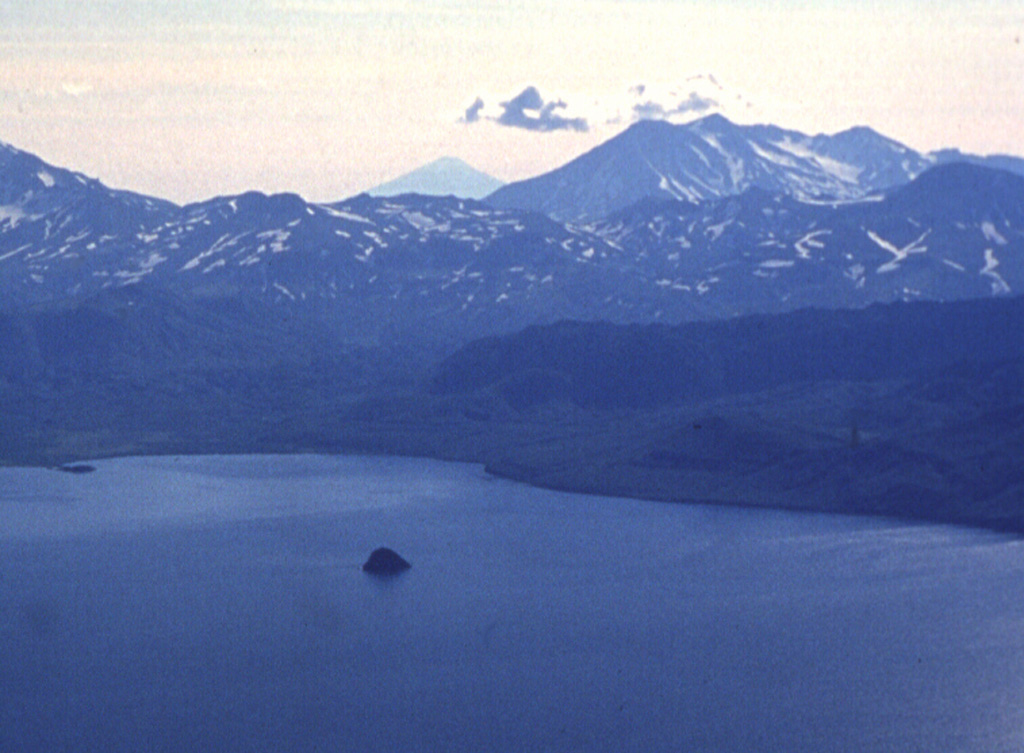 Koshelev (upper right) is one of the southernmost active volcanoes on the Kamchatka Peninsula, seen here SW of the Kurile Lake caldera. It contains four main cones constructed along an E-W line over a Pleistocene edifice with the central and highest peak being the youngest. An explosive eruption occurred at the end of the 17th century. Alaid, the northernmost volcano of the Kuril Islands, is the peak on the left horizon. Photo by Nikolai Smelov, 1996 (courtesy of Vera Ponomareva, Inst. Volcanic Geology & Geochemistry, Petropavlovsk).