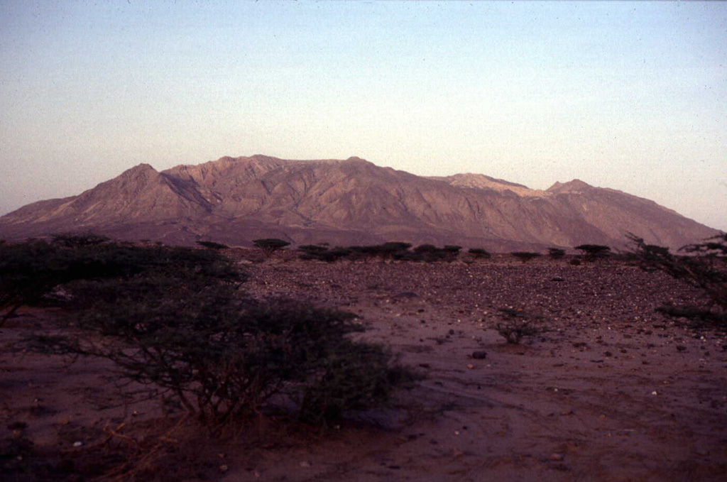 The elongated Alid volcano, which sits on the axis of the Danakil spreading center, is seen here from the W. Most of the flanks of the volcano in this view are composed of dipping rhyolitic lava flows; the light-colored area along the right skyline is rhyolitic pumice. The summit of the volcano is elongated in an E-W direction and contains a 1 x 1.5 km wide, 100-m-deep crater at the western end. Vast lava fields originating from fissure vents in the Alid graben extend to the NW and SE of the volcano. Vigorous fumarolic activity continues at Alid. Photo by Wendell Duffield, 1996 (U.S. Geological Survey).
