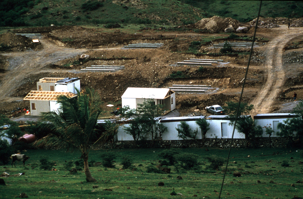 The Soufrière Hills eruption progressively impacted larger proportions of Montserrat.  The eruption imposed severe hardships as more and more of the heavily populated southern half of the island became uninhabitable.  Eventually more than half of the island's 11,000 residents left to other West Indies islands, or  to England, but more than 4000 people elected to remain on Montserrat.  These prefabricated houses were being constructed in September 1997 to house refugees at Davy Hill, on the northern side of the island. Photo by Lydia Mihelic Pulsipher, 1997 (University of Tennessee).