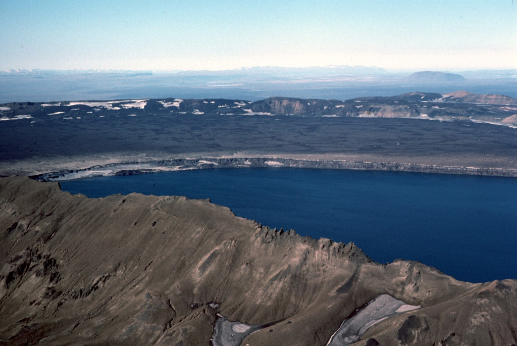Askja's largest historical eruption occurred in 1875. Subsidence of the caldera continued for 40-50 years after the eruption and resulted in the formation of Askja's inner caldera, now filled by Öskjuvatn lake, seen here from the SE. The flat, lava-covered floor of the main caldera can be seen beyond the lake, encircled by the caldera rim.  Photo by Michael Ryan, 1984 (U.S. Geological Survey).