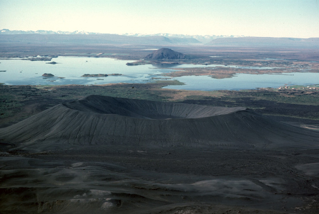 The Hverfjall tuff ring (foreground) developed during phreatomagmatic explosions at the southern end of a 23-km-long fissure. This tuff ring is the largest of the Krafla volcanic system, with a crater about 1 km wide. Lava-dammed Mývatn lake, in the background to the west, provides wildlife habitat and is renowned for its diversity of bird life. The lake has formed on lava flows from nearby Heiðarsporðar volcano, which surround Vindbelgjarfjall, the dome seen on the far side of the lake. Photo by Michael Ryan, 1984 (U.S. Geological Survey).