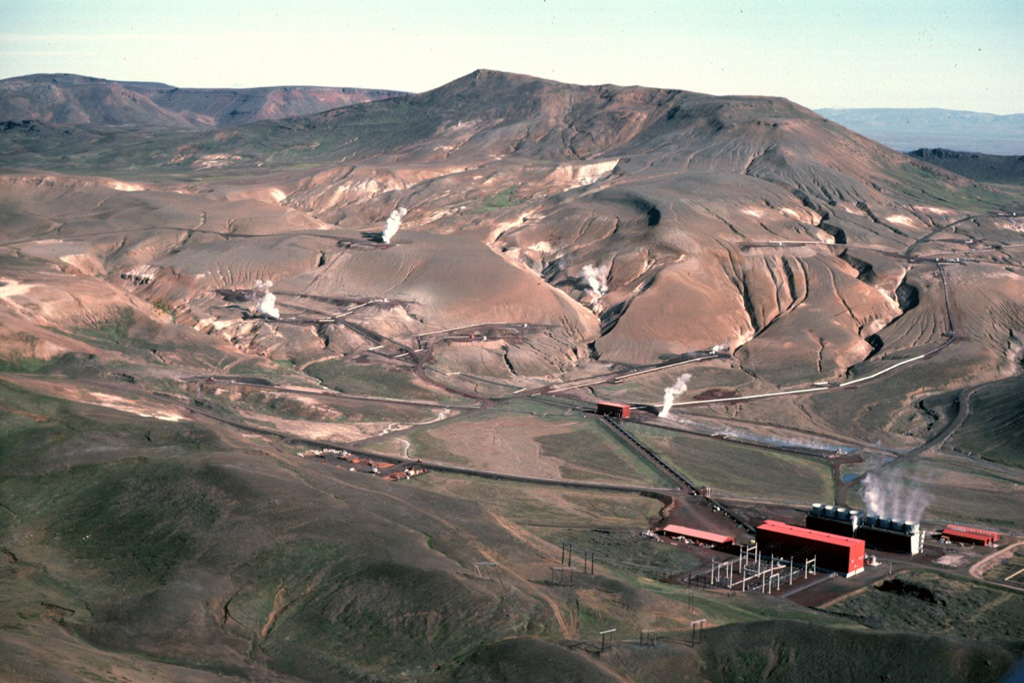 This power plant (lower right) is part of a large geothermal development south of the Krafla caldera. The Krafla ridge in the background is seen from the SW, with steam rising from the geothermal wells. The northeastern caldera rim forms the horizon on the left. Photo by Michael Ryan, 1984 (U.S. Geological Survey).