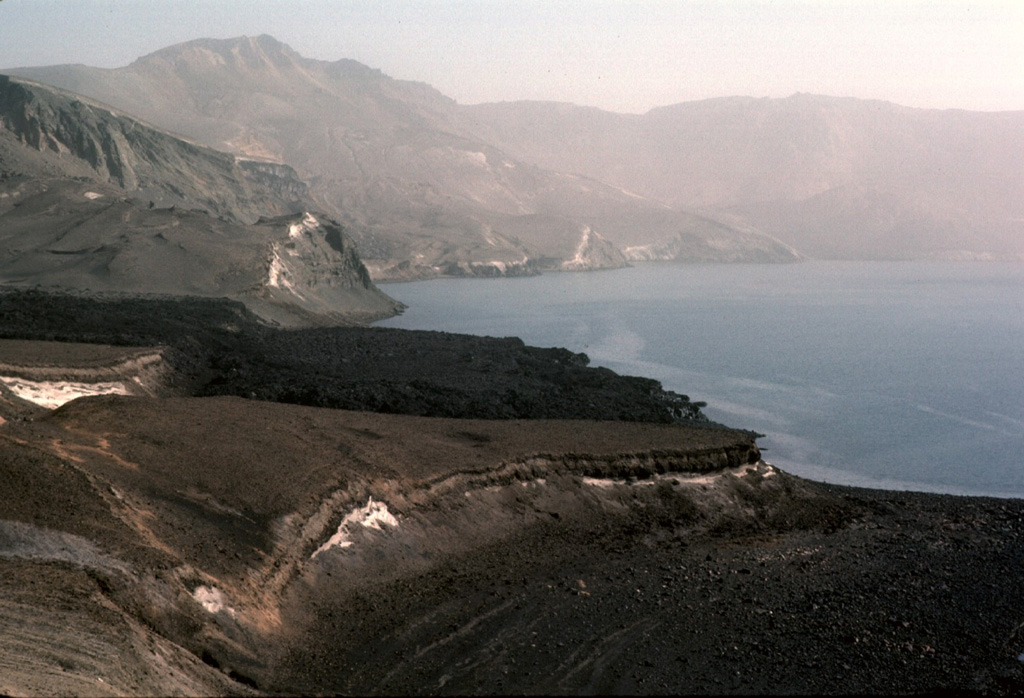 The dark Batshraun lava flow descending from the left into Öskjuvatn lake was erupted during 1921. The lava flow originated from a vent below the NE rim of Askja's central caldera, and flowed over the low rim of the younger 1875 caldera into the lake. The lava flow was the first of several during the 1920's that flowed into the NE, SE, and W sides of Öskjuvatn lake. Photo by Michael Ryan, 1984 (U.S. Geological Survey).