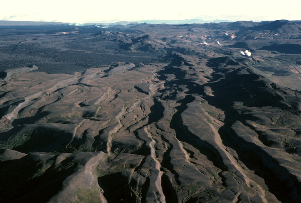 This north-looking view along fissures cutting Iceland's Krafla volcano illustrates crustal spreading processes where the Mid-Atlantic Ridge rises above sea level. The prominent horst-and-graben structures seen here are the result of repeated episodes of extensional rifting during which crustal blocks moved east and west, perpendicular to the line of faults. A period of pronounced crustal rifting occurred from 1975 to 1984, accompanied by nine small fissure eruptions. Steam can be seen in the upper left, rising above an active eruptive fissure in this September 1984 photo. Photo by Michael Ryan, 1984 (U.S. Geological Survey).