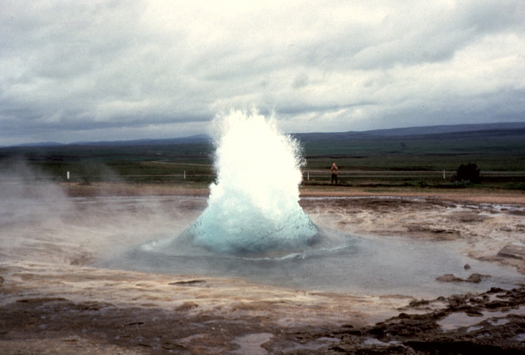 Iceland's largest geysers are located in the Haukadalur basin, part of the Geysir volcanic system, just east of the southern end of the Oddnyjarhnjukur-Langjokull fissure system. Here, the Strokkur geyser can be seen just as a burst of boiling water and steam erupts from a pool. This geyser erupts about every 10 minutes, producing a short-lived fountain that usually reaches about 20 m. Photo by Bill Rose, 1975 (Michigan Technological University).