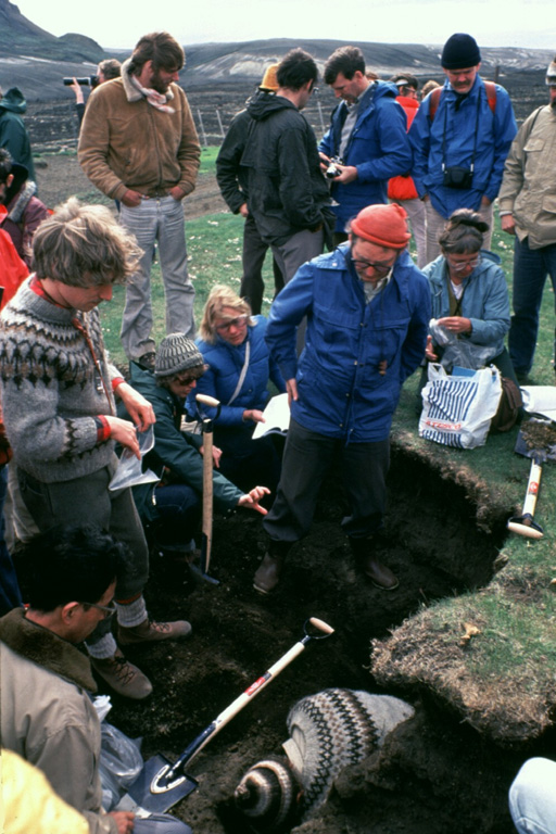 Icelandic volcanologist Sigurdur Thorarinsson (right center, with red cap) discusses ash layers exposed in an excavated pit with an international group of volcanologists on a field trip. Thorarinsson pioneered the technique of tephrochronology, and his detailed studies of tephra layers from Hekla demonstrated the value in determining the relative ages of ash layers by their stratigraphic position between dated horizons. Photo by Bill Rose, 1980 (Michigan Technological University).