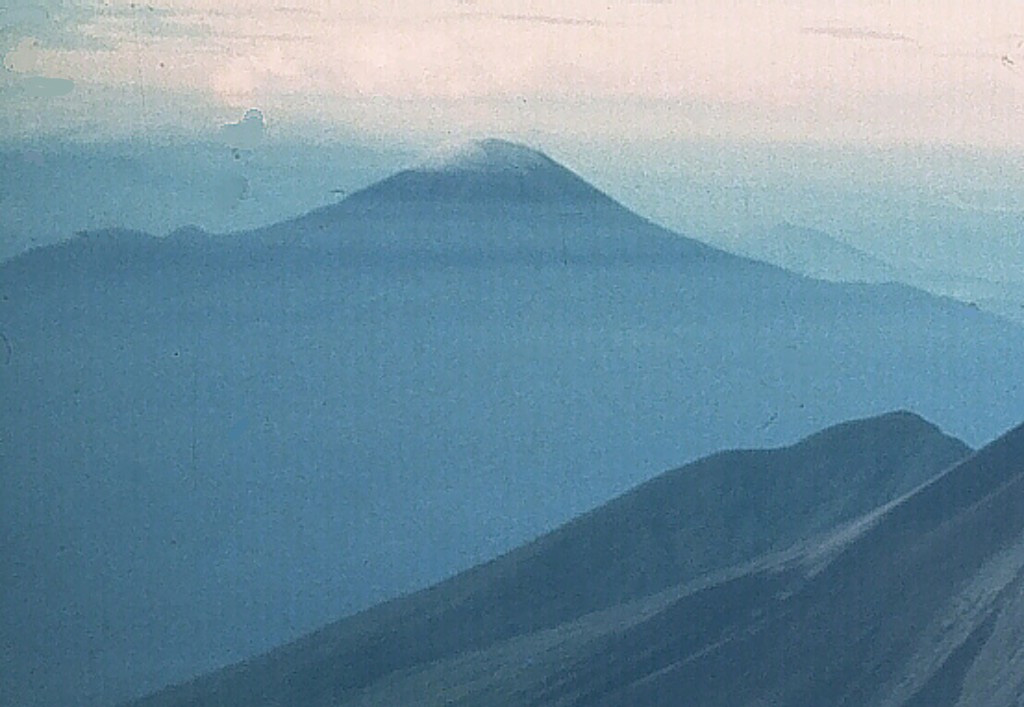 Bamus is seen here from the NE beyond the upper slopes of Ulawun. These two volcanoes are the highest in the 1,000-km-long Bismarck volcanic arc. Bamus is covered by rainforest and contains a summit crater filled with a lava dome. A smaller cone is located on the S flank, and a prominent 1.5-km-wide crater with two small adjacent cones is situated halfway up the SE flank. Photo by Wally Johnson (Australia Bureau of Mineral Resources).