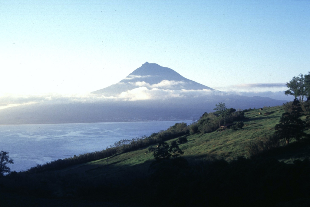 Pico volcano, the highest in the Azores, is located across a narrow 6-km-wide channel southeast of Fayal Island. From this direction, the stratovolcano appears to be a symmetrical cone, but it lies at the far western end of an elongated chain of cones that forms a roughly 800-m-high ridge extending ESE across Pico Island. Fumaroles are located near a small cone filling the summit crater, but eruptions recorded since 1562 CE have all occurred from flank vents. Photo by Rick Wunderman, 1997 (Smithsonian Institution).
