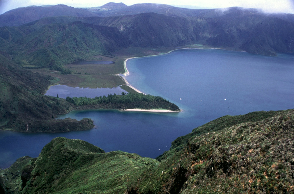 Lagoa do Fogo, seen here from the west, partially fills the younger of two Pleistocene calderas on Agua de Pau stratovolcano in central Sao Miguel Island. The walls of the caldera surrounding the lake rise to a maximum of about 370 m above the surface. Eruptions have occurred both inside the caldera and on the flanks, where multiple cones and domes can be found. Two major explosive eruptions have occurred in the Holocene from the caldera: the Ribeira Cha (8,000 to 12,000 years ago) and Fogo A (about 4,600 years ago).  Photo by Rick Wunderman, 1977 (Smithsonian Institution).