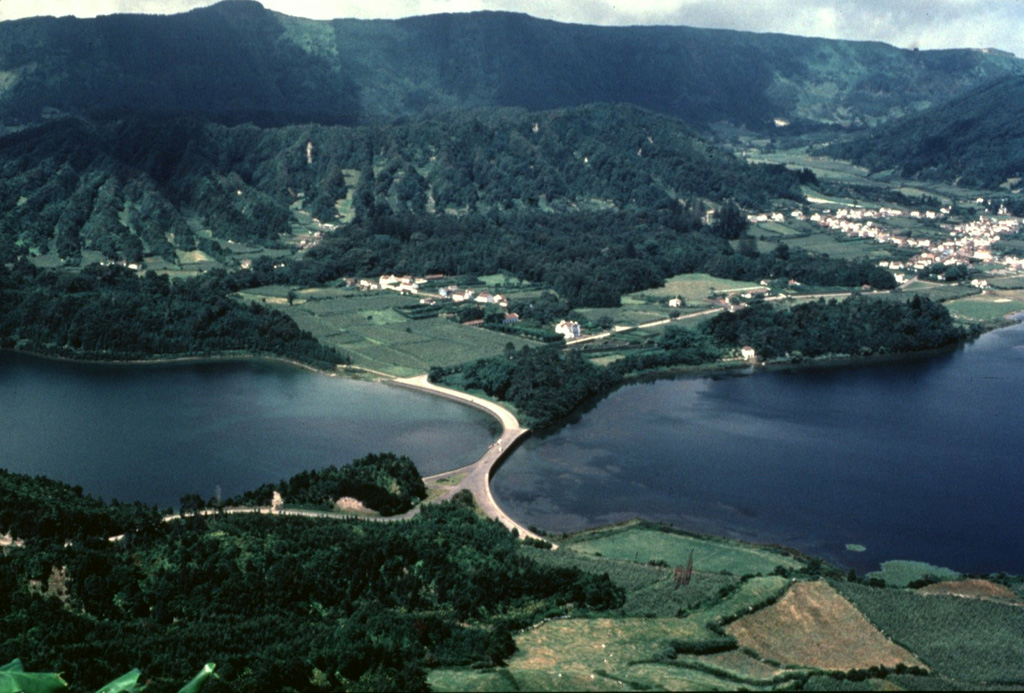 A highway bridge spans the junction of Lagoa Verde (left) and Lagoa Azul (right) lakes on the floor of Sete Cidades caldera.  The erosionally furrowed wall of Caldeira Seca, the youngest of a circular group of post-caldera pyroclastic cones constructed within 5-km-wide Sete Cidades caldera, rises beyond the two lakes.  The town of Sete Cidades (upper right) occupies the caldera floor between Caldeira Seca and another youthful pumice cone, Caldeira do Alferes. Copyrighted photo by Katia and Maurice Krafft, 1980.