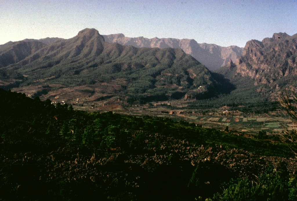 The steep-walled Caldera de Taburiente is the most prominent feature of La Palma island.  The caldera extends 10 km in a NE-SW direction and is breached to the sea on the SW side through a narrow notch at the left.  Historical eruptions on La Palma have been restricted to a series of fissures and cones along a N-S-trending dorsal ridge extending to the southern tip of the island. Copyrighted photo by Katia and Maurice Krafft, 1977.