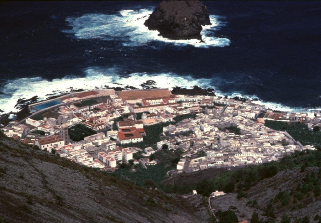 The town of Garachico on the northwestern coast of Tenerife Island occupies a lava delta created during an 18th-century eruption.  The Garachico cinder cone, which was formed during the 1706 eruption, produced a 7-km-long lava flow that descended nearly 1400 m to the sea, destroying much of the village of Tanque as well as the town and port of Garachico.  The Roque de Garachico island at the top of the photo predates the lava flow. Copyrighted photo by Katia and Maurice Krafft, 1977.