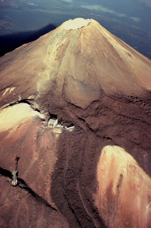 Trachytic lava flows with prominent lateral levees descend from the summit of Pico de Teide volcano and spill over the rim of an older crater.  The pylon at the lower left and the building at left-center mark the upper part of an aerial cable car line that provides access to the 3715-m-high summit of Pico de Teide, the highest peak in the Atlantic Ocean.   Copyrighted photo by Katia and Maurice Krafft, 1977.