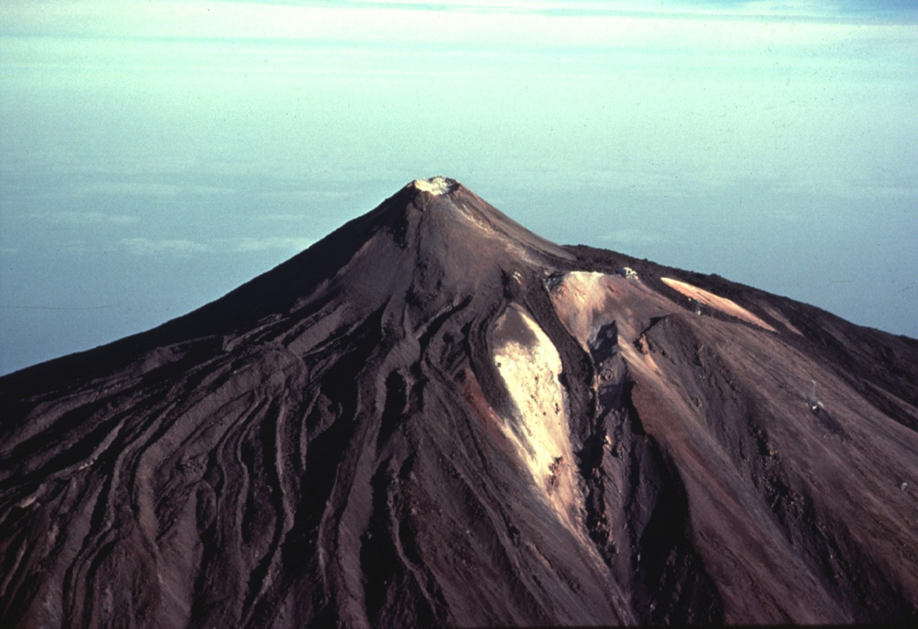 Steep-sided Pico de Teide rises to 3715 m on SW Tenerife Island.  The summit cone is capped by a small 70-m-wide crater and was constructed within a larger crater, whose outer slopes form the light-colored areas at the right.  A dramatic complex of overlapping obsidian-bearing lava flows with prominent levees descends from the summit and drapes the western flanks of the volcano.  The age of the lava flows is not known, but they represent some of the most recent eruptive activity on Tenerife. Copyrighted photo by Katia and Maurice Krafft, 1977.
