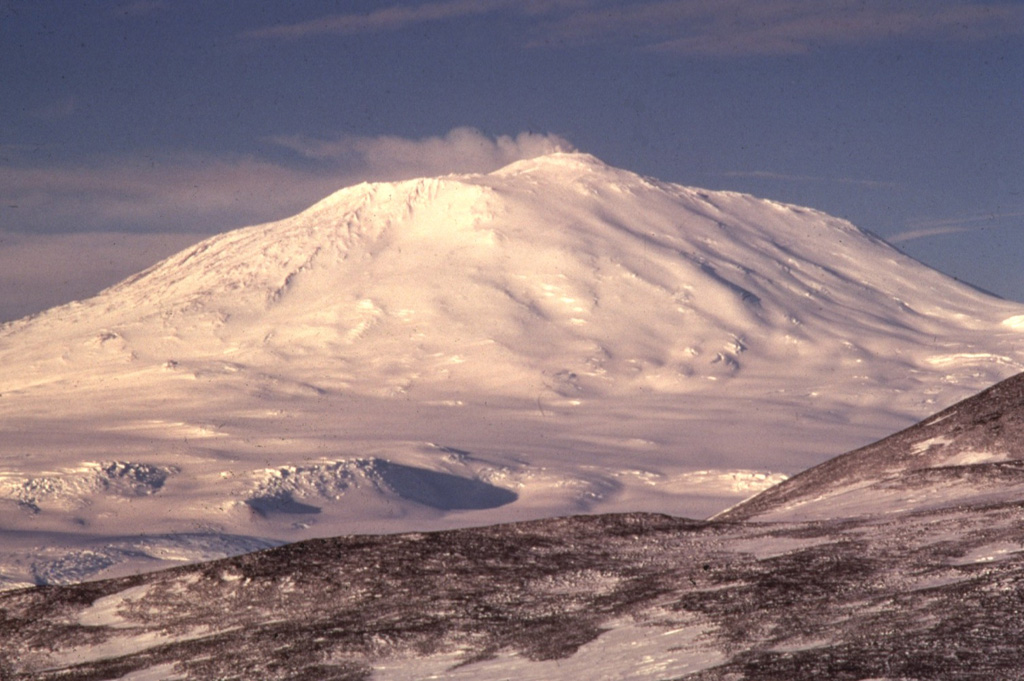 Mount Erebus is seen here from the SW near the McMurdo research station on Ross Island and the world's southernmost active volcano. The summit has a 500 x 600 m wide, 110-m-deep crater that contains an active lava lake. The glaciated volcano was erupting when first sighted by Captain James Ross in 1841. Continuous lava lake activity has been documented since 1972, punctuated by occasional Strombolian explosions that eject bombs onto the crater rim. Photo by Richard Waitt, 1972 (U.S. Geological Survey).