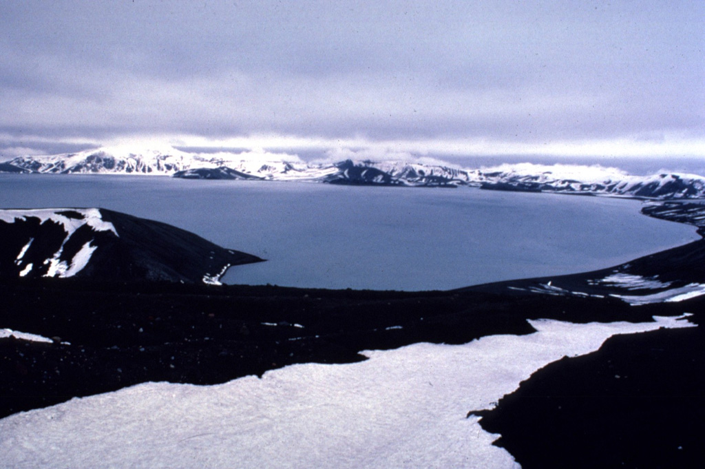 The western wall of Deception Island caldera is visible across Port Foster caldera bay from the Chilean Antarctic research station at Pendulum Cove.  Eruptions took place at Telefon Bay, on the opposite shore of the flooded caldera during 1967 and 1970.  An eruption in 1969 completely destroyed the Chilean base.  Copyrighted photo by Katia and Maurice Krafft, 1984