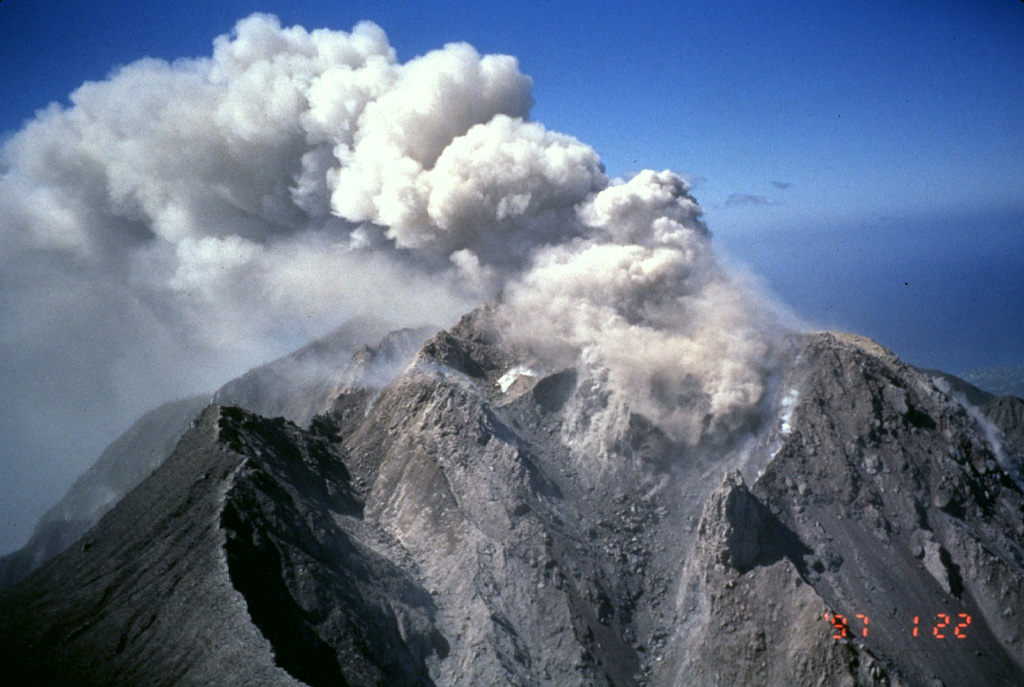Three generations of lava-dome growth can be seen in this January 27, 1997 aerial photo of Soufrière Hills volcano.  Ash is venting from a small dome that began growing in December 1996 within a scarp formed by collapse of an October 1996 lava dome.  The October dome in turn was constructed within a scarp whose southern wall forms the cliff at the lower left.  This outer scarp was formed by collapse of a pre-September 1996 lava dome.  Photo by Mark Davies, 1997 (Montserrat Volcano Observatory).