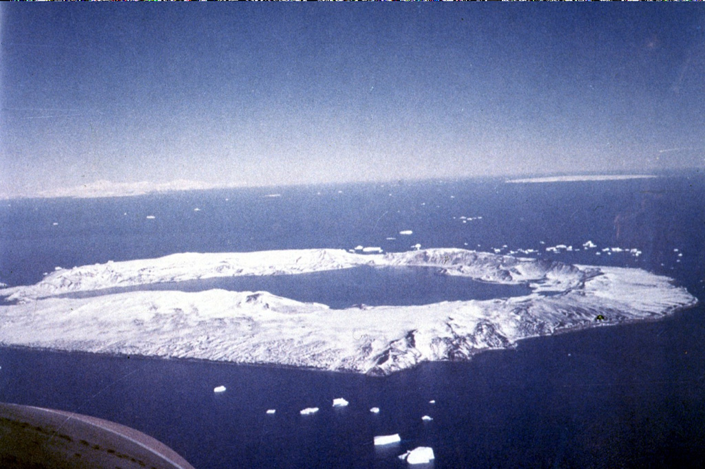 Deception Island in Antarctica contains a 7-km-wide caldera flooded by the sea. A narrow passageway named Neptune’s Bellows cuts through the caldera wall to the left. Numerous vents located along the caldera ring fractures around the low, 14-km-wide island have been active during historical time. Maars produced by magma-water interaction occur across the shores of the 190-m-deep Port Foster. Photo by Juan Bastias (published in González-Ferrán, 1995).