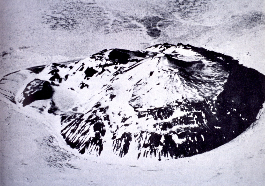 The small 1.8 x 2.2 km Paulet island, seen here in an aerial view from the west, is composed of lava flows capped by the Volcán Paulet and Volcán Larsen scoria cones. The largest and youngest cone, Paulet, contains a small circular summit crater of less than 100 m diameter. A small lake fills a maar-like depression called Volcán Andersson (center left). Photo published in González-Ferrán (1995).