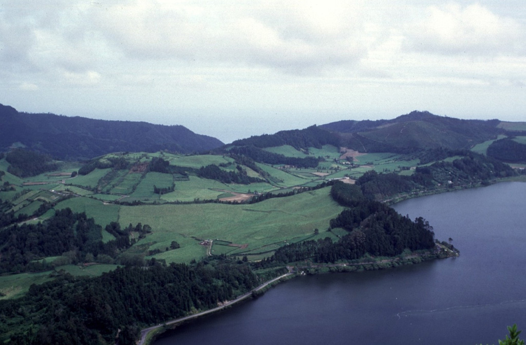 The low hill covered by fields (left center) is Pico do Gaspar lava dome, surrounded by a low tuff cone. The Lagoa das Furnas lies to the west (right) and the eastern caldera wall can be seen in the left background. The Pico do Gaspar dome has been the site of two eruptions, including in about 1439-1443 CE; descriptions suggest an initial explosive phase producing ash, followed by lava dome formation.  Photo by Rick Wunderman, 1997 (Smithsonian Institution).