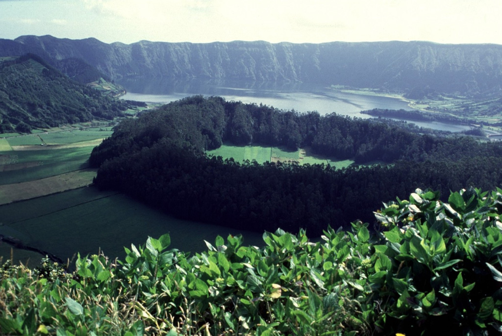 The tree lined, approximately 500 x 700 m, Caldeira Seca pumice ring (center) on the floor of the Sete Cidades caldera, with Lagoa Azul and the northeast wall of the caldera in the background. The southeastern flank of the Calderia do Alferes is seen in the upper left. Caldeira Seca formed during a 15th-century phreatomagmatic eruption in which large amounts of pumice ash, lapilli and blocks were erupted. Photo by Rick Wunderman, 1997 (Smithsonian Institution).