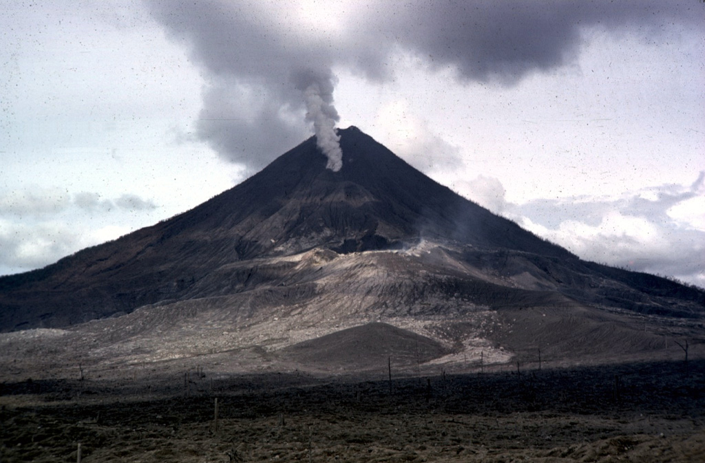 The initial explosions of the 1968 Arenal eruption took place at three craters located from the summit down the west flank. Crater A is visible in the sunlight at the center of the photo; this was the source of the devastating explosions on 29 July. A gas plume rises from Crater B, obscuring Crater C behind it. Lava effusion from Crater C began in September and continued for many years.   Photo by William Melson, 1968 (Smithsonian Institution).