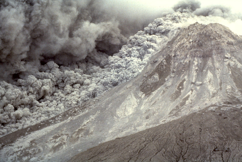 An ash plume expands above a pyroclastic flow sweeping down the E flank of the Soufrière Hills summit lava dome on 16 January 1997. The pyroclastic flow descended the Tar River valley to the sea, covering the new delta with new material that included blocks up to 5 m in diameter. Photo by Richard Herd, 1997 (Montserrat Volcano Observatory).
