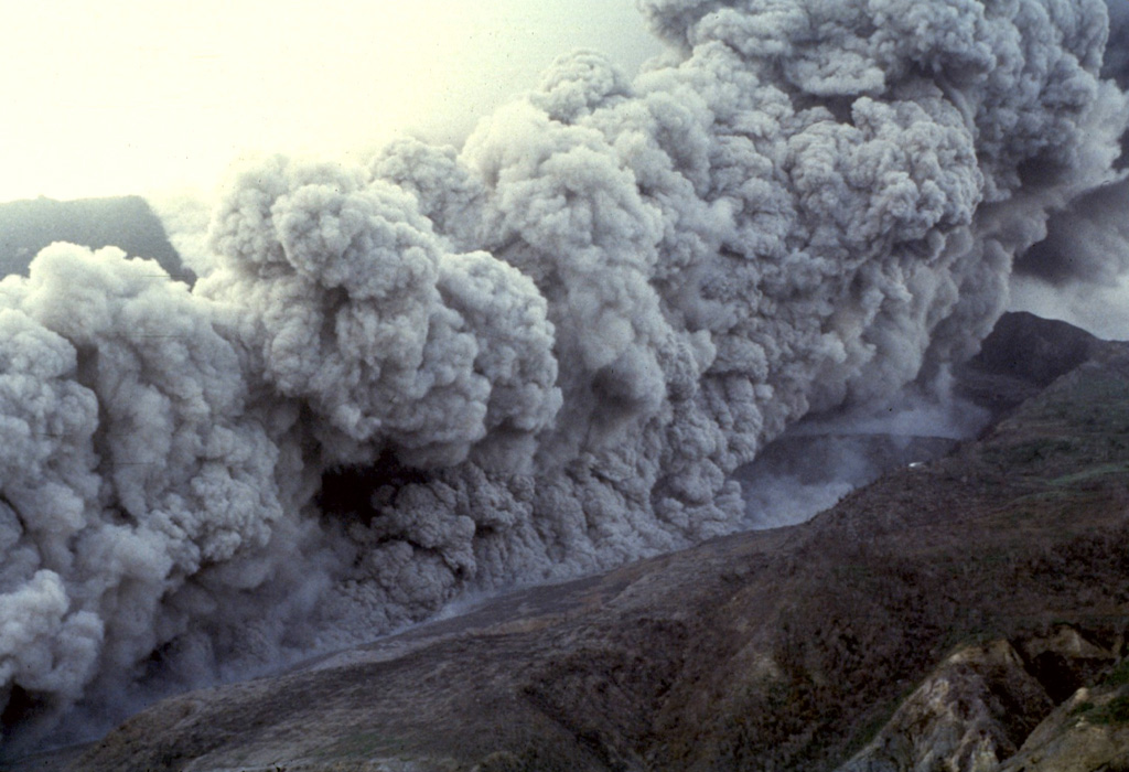 A pyroclastic flow sweeps down the floor of the Tar River valley on the eastern flank of Soufrière Hills volcano on January 16, 1997.  The Tar River Estate house, which had been damaged by earlier eruptions, is the white dot on the ridge at right center.  The January 16 pyroclastic flow  was the largest to date during the eruption.  The pyroclastic flow traveled about 3.5 km into the sea beyond the new delta formed at the mouth of the Tar River valley.  Photo by Richard Herd, 1997 (Montserrat Volcano Observatory).