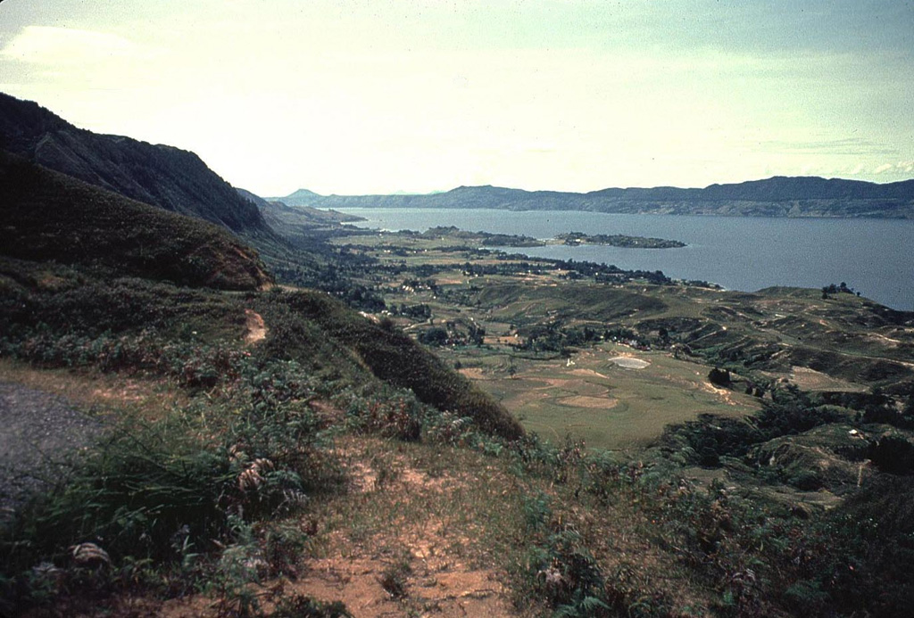 The eastern wall of the Toba caldera forms the horizon across Lake Toba from Samosir Island in the foreground. The small Tuk-Tuk peninsula (center) extends into the lake from the 630 km2 island. The small conical peak on the horizon at left-center is Tandukbenua volcano, which may have erupted only a few hundred years ago. Photo by Bill Rose, 1982 (Michigan Technological University).