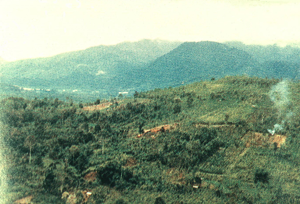 Kunyit volcano rises above fields near its eastern flank. The summit has two craters open to the south and the uppermost crater contains a small crater lake. The age of the latest eruptive activity from Kunyit is not known, although fumarolic activity occurs at the youngest summit crater. Photo courtesy of Volcanological Survey of Indonesia, 1981.