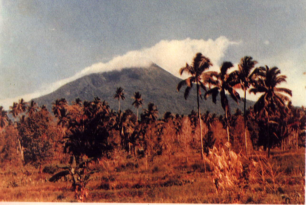 Weather clouds drape the summit of Gunung Klabat, an isolated symmetrical stratovolcano that rises to 1995 m near the eastern tip of the northern arm of Sulawesi.  Klabat, rising above the farming village of Tatelu below its NW flank, has a shallow lake in its 170 x 250 m summit crater.  No verified historical eruptions have occurred from Klabat volcano, the highest peak in northern Sulawesi.   Photo by S. Wikartadipura, 1981 (Volcanological Survey of Indonesia).