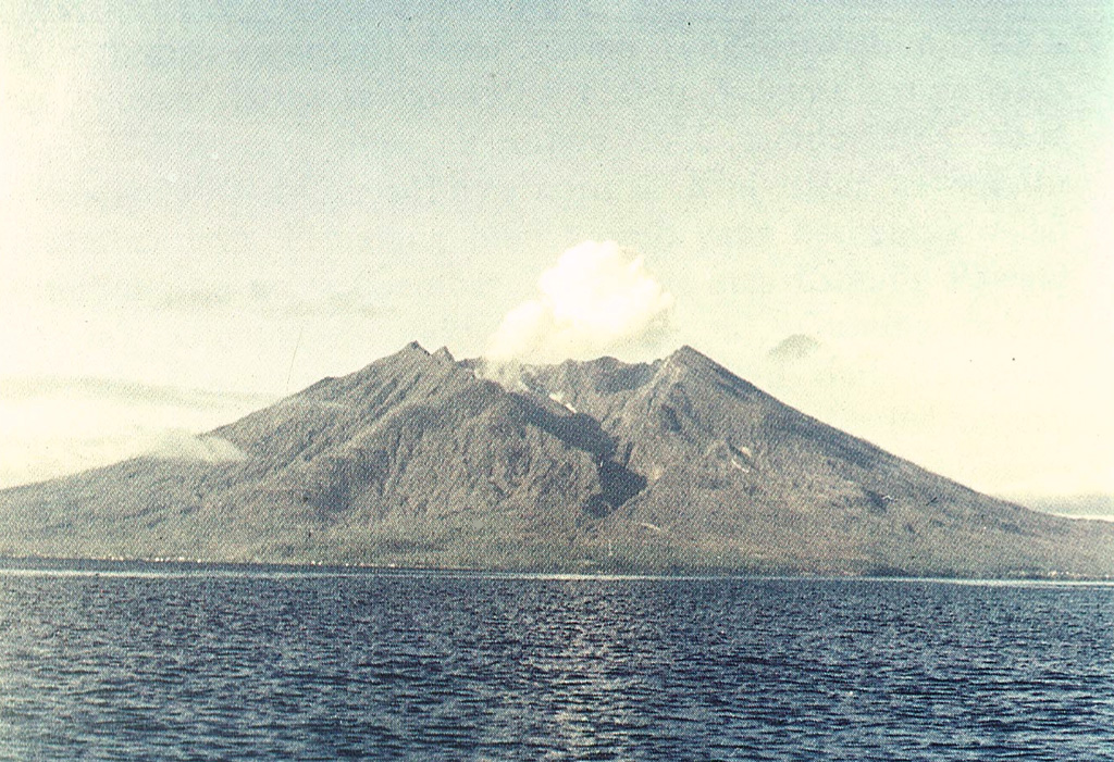 Makian volcano forms a 10-km-wide island near the southern end of a chain of volcanic islands off the western coast of Halmahera.  The northern of two prominent valleys that extend from the summit is prominent in this photo.  The large 1.5-km-wide summit crater containing a small lake on the NE side gives the 1357-m-high peak a flat-topped profile.  Violent eruptions from Makian volcano, also known as Kie Besi, have devastated villages on the island. Photo by Sumaryono (Volcanological Survey of Indonesia).