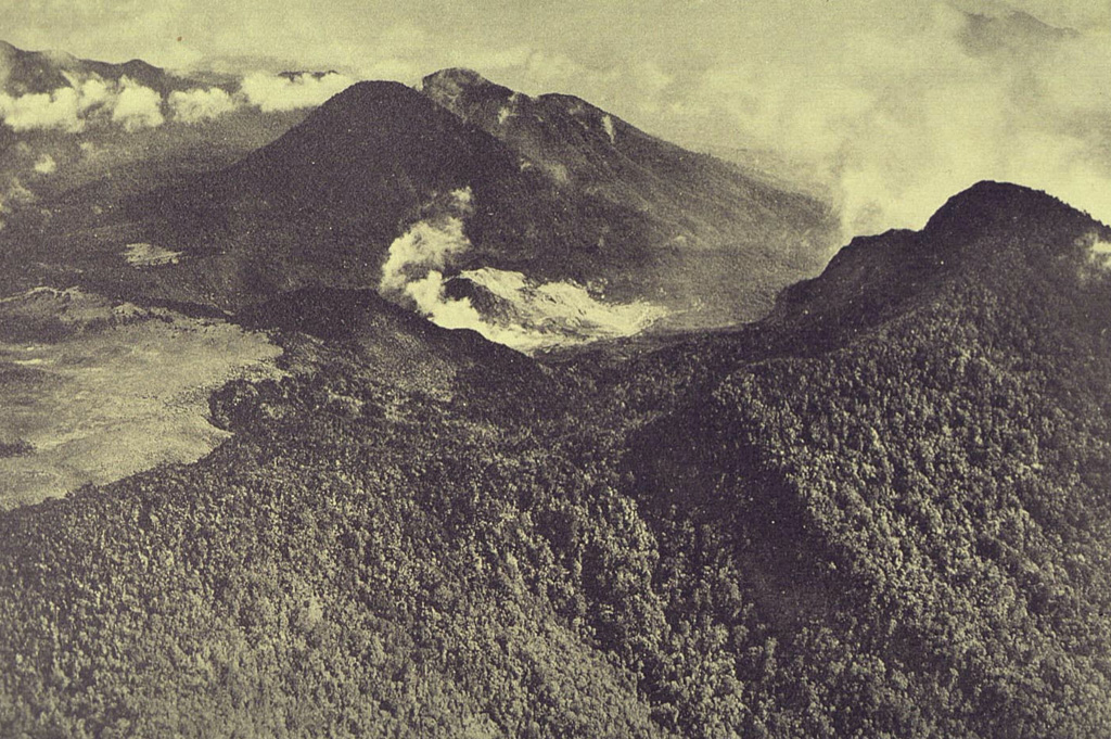 An aerial view from the south shows the complex summit of Papandayan volcano. The lighter-colored, flat area at the left is Alun-Alun, the uppermost of four summit craters. A gas plume rises from a hydrothermal area within the area remaining after the collapse of the summit in 1772. The forested peak at the right is the eastern summit. The two peaks at the upper left are Gunung Puntang and Gunung Jaja. Photo published in Taverne, 1926 