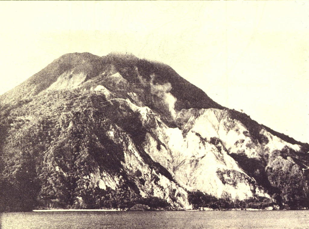 A fumarole plume (right-center) rises above the steep SE slopes of Nila volcano, also known as Laworkawra or Lawarkawra.  A remnant of the rim of a 5-km-wide caldera forms the forested slope at the left.  The 781-m-high summit above it is a post-caldera cone that fills much of the caldera and extends to the sea at the right.  Phreatic eruptions from Gunung Nila have occurred from summit vents and flank fissures during historical time.  Photo by Ruska Hadian, 1975 (published in Kusumadinata 1979, 