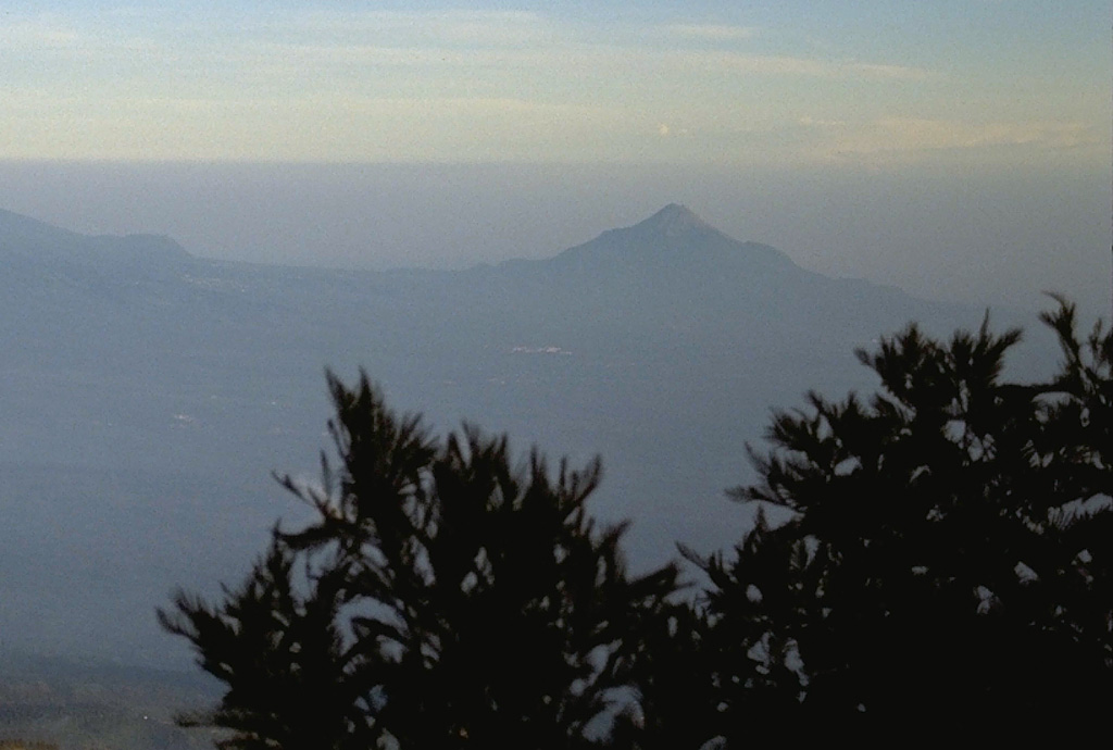 Gunung Penanggungan, seen here from Tengger caldera to its east, was constructed immediately north of the Arjuno-Welirang massif with its flanks forming the ridge at the left. Lava flows from flank vents give the volcano an irregular profile. Lava flows have descended all flanks of the volcano and pyroclastic flow deposits form an apron around it. Photo by Lee Siebert, 1995 (Smithsonian Institution).