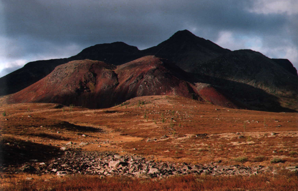 The Ulug-Arginsky scoria cone, seen here from the north in the sunlight in the center, is part of the Azas Plateau volcanic field west of the SW tip of Lake Baikal. Large granitic erratics (boulders emplaced by glaciers) were deposited on the surface, and lava flows from the cone are glacially eroded and overlain by moraines. The Azas Plateau volcanic field covers an area of about 1,500 km2. Some basaltic lava flows in broad glacially carved valleys are unglaciated and of probable Holocene age. Photo by Sergei Arzhannikov, 1997 (Siberian Branch, USSR Academy of Sciences).