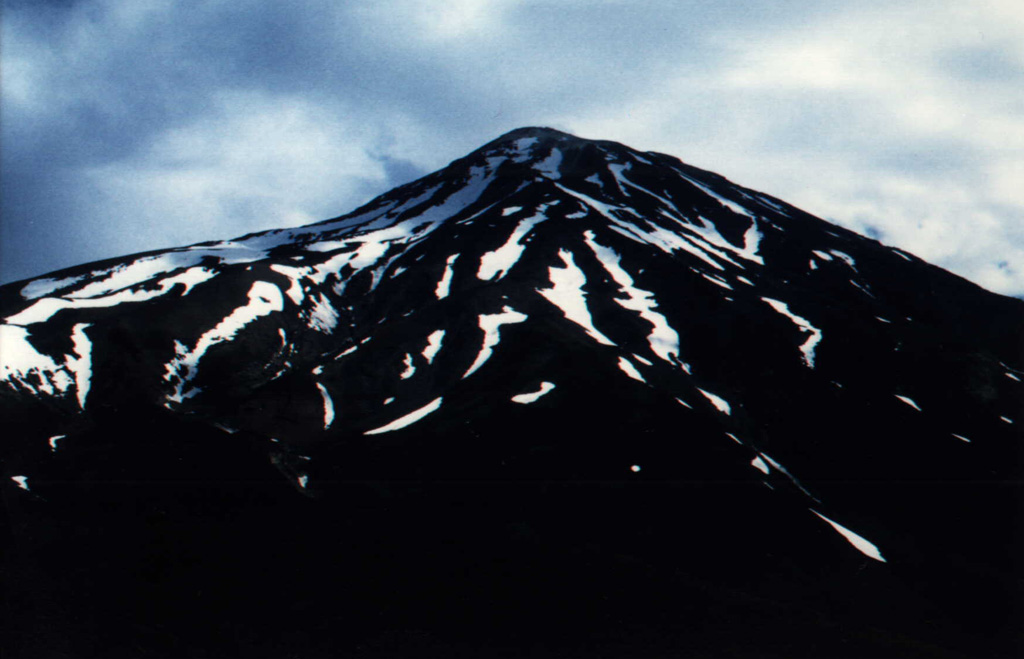 Damavand volcano in the Elbruz mountains, about 80 km NE of Iran's capital city Tehran, is seen here from the S flank, at an elevation of 3,500 m. The summit of the stratovolcano contains a well-preserved, 150-m-wide crater with a small frozen lake. Despite its elevation above 5,000 m, the region is too arid to support permanent glaciers. Recent lava flows from the summit and flank vents cover the W side of the volcano. Photo by J. Sesiano, 1998 (University of Geneva).